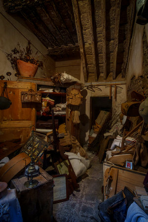 Dark storeroom, exposed beams, antique furniture, stacked fabric, tools, and household items.の写真素材
