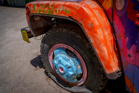 Close up of a deflated wheel on a painted rusty truck parked in bright sunlight.の写真素材