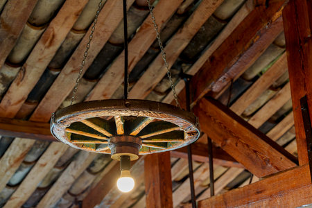 Rustic wagon-wheel chandelier hanging from wooden beamed ceilingの写真素材