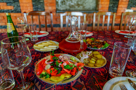 Plates of fresh tomato salad, potatoes, cheese, and eggplant surround a clay wine decanterの写真素材
