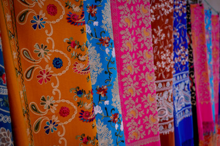 Brightly colored embroidered textile panels with floral designs displayed together in fabric shopの写真素材