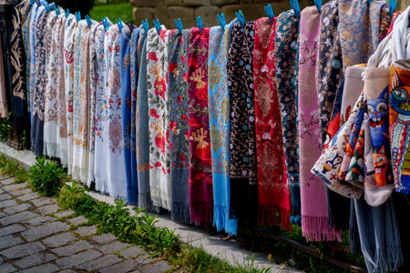 Row of bright patterned scarves with fringes hanging on rail at outdoor souvenir marketの写真素材