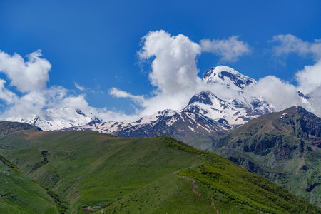 Majestic Mount Kazbek dominates the skyline above lush rolling hills and grassy summer slopes.