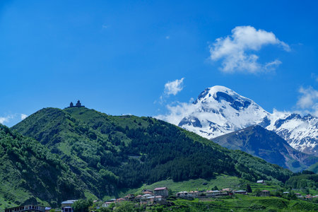 Gergeti Trinity Church crowns a green hill with snowy Mount Kazbek rising dramatically behind.
