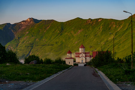 A small Georgian church sits at the end of a quiet mountain road at sunset.