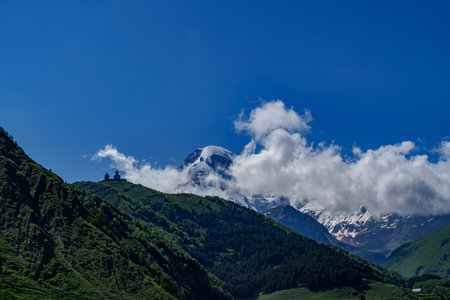 Gergeti Trinity Church stands on a green ridge as clouds swirl around distant Mount Kazbek.