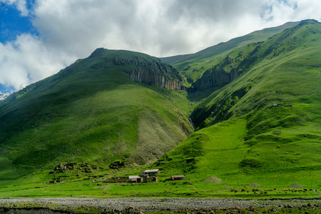 A tiny farm settlement nestles in a bright green valley below rugged, cliff-topped hillsides.