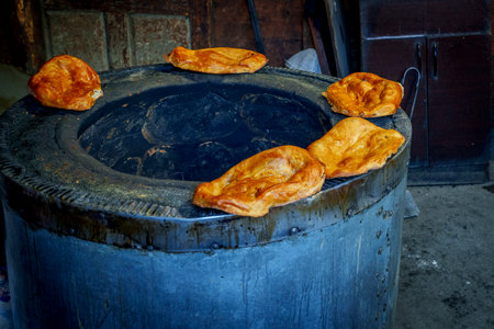 Freshly baked Georgian bread pieces rest on the rim of a hot clay tone oven.