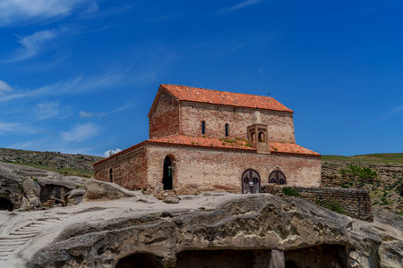Ancient brick church with red roof stands above rock caves in historic Uplistsikhe cave city.