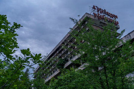 Long derelict hotel block emerges from dense trees, topped by a rusted metal rooftop sign.の写真素材