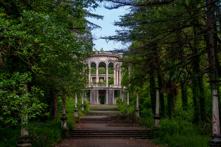 Overgrown trees flank a grand stairway leading to a derelict arched pavilion deep in the park.の写真素材