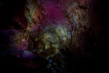 Vast cavern with colorful lights painting rock ceiling purple and gold above small walkway belowの写真素材