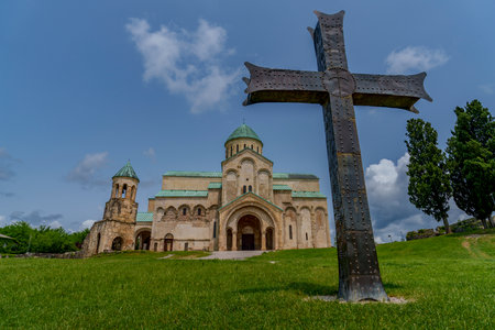 Impressive hilltop cathedral framed by monumental iron cross, under blue sky and scattered clouds