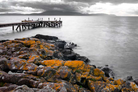 A pier by the sea with orange rocks on the shoreの写真素材
