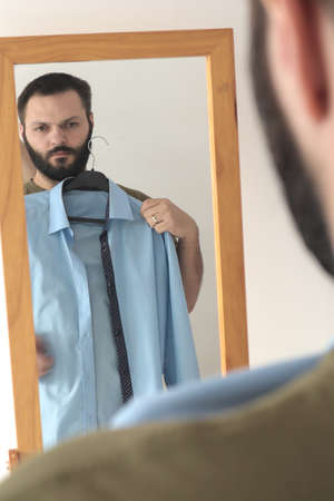Man trying on smart shirts against a mirror at the morning, before work. Selective focus.の写真素材