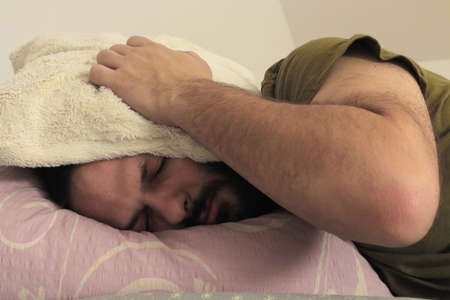 man covering his ears with pillow at the morning. selective focus.の写真素材