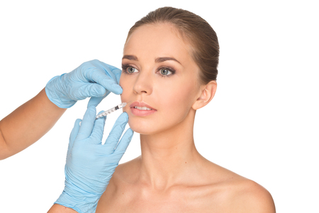 Attractive young woman gets cosmetic injection , isolated over white background. Doctors hands making an injection in face. Beauty Treatment.の写真素材