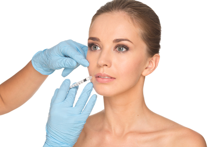 Attractive young woman gets cosmetic injection , isolated over white background. Doctors hands making an injection in face. Beauty Treatment.の写真素材