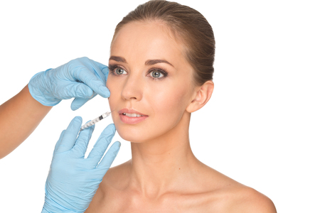 Attractive young woman gets cosmetic injection , isolated over white background. Doctors hands making an injection in face. Beauty Treatment.の写真素材