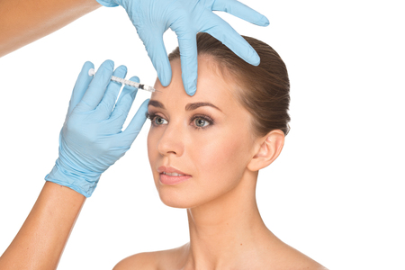 Attractive young woman gets cosmetic injection , isolated over white background. Doctors hands making an injection in face. Beauty Treatment.の写真素材