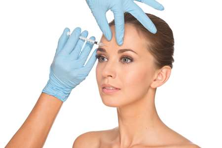 Attractive young woman gets cosmetic injection    , isolated over white background. Doctors hands making an injection in face. Beauty Treatment.の写真素材