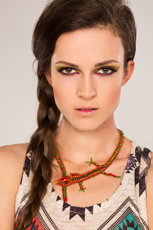 Brunette looking at camera on gray background with ethnic make-up and lizard jewellery on the neckの写真素材