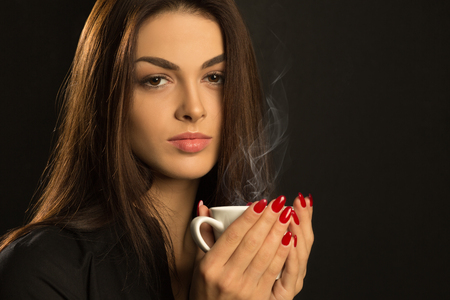 Young brunette woman with cup of coffee on a dark backgroundの写真素材