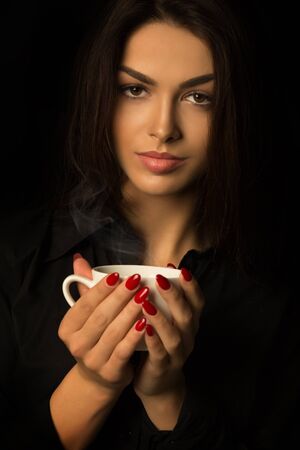 Young brunette woman with cup of coffee on a dark backgroundの写真素材