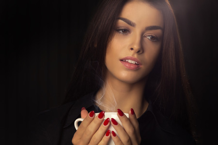 Portrait of sexy woman enjoying a hot cup of coffee on a dark backgroundの写真素材