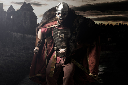 Screaming viking warrior with sword, armour and helmet before castle and sunsetの写真素材