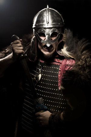 Screaming viking warrior with sword, armour and helmet over black backgroundの写真素材