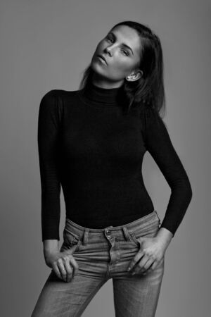 Portrait of sexy, thoughtful brunette in black sweater, jeans with earrings over gray backgroundの写真素材