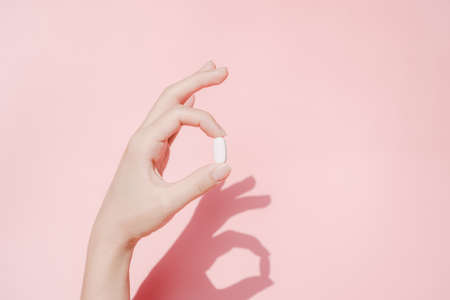 Woman's hand holding white pill over pink backgroundの写真素材