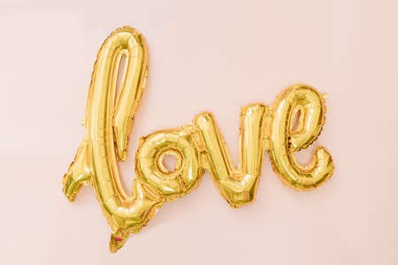 Word love made of gold balloons over pink background