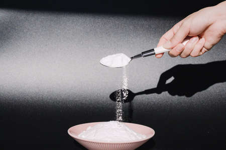 Hand pouring white powder from spoon in front of black backgroundの写真素材