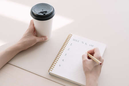 Hand writing New Year's resolutions in a notebook with takeaway coffeeの写真素材