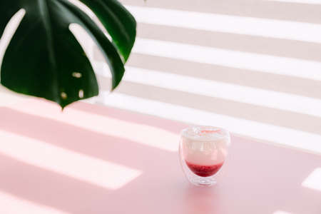 Glass cup with jam on pink table and green monstera leaf in sunlightの写真素材