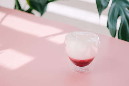 Cocktail in a transparent glass on a pink background with a green plant.の写真素材