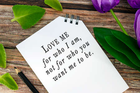 Motivational quote on notepad with flowers on wooden desk - Love me for who i am not for who you...
