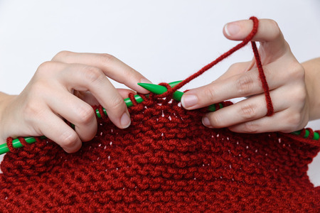 Girl's hands are knitting a red muffler out of wool with green knitting needles.の写真素材