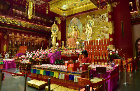 Singapore - February 2015.Buddhist temple interior with altar and the sacred figurines and lights.The young man laying the lights on the altar.Editorial.Horizontal view.のeditorial素材
