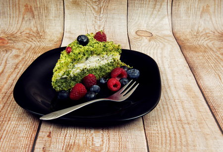 Black plate with a piece of spinach cake, forest fruit and forks for cakes, on the background of wooden planks.Horizontal view.の写真素材