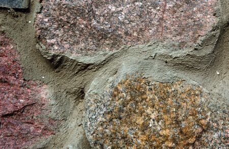 Fragment of a stone wall with large boulders connected with cement. Close, horizontal view