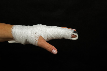 Women hand with finger crossed over rail stabilizing wrapped in elastic bandage, injury finger on a black background. Close, horizontal view.の写真素材