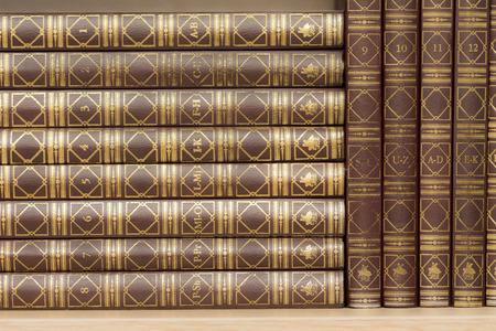 Encyclopedias arranged alphabetically standing on a wooden shelfの写真素材