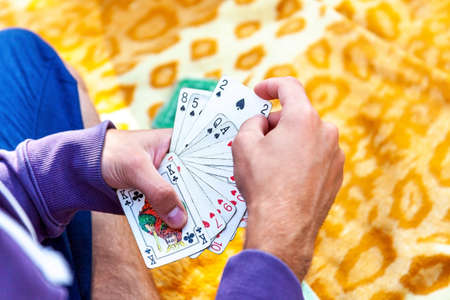 Young man in casual clothing playing cards sitting on a blaket outside, hands closeup, picking one...
