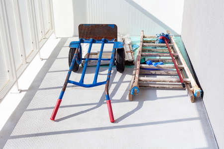 Handtruck and a wooden painter ladder and a mop laying on the white balcony. House or flat under...