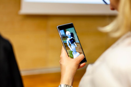 Cracow, MaÅopolska / Poland - September 4 2019: Woman photographing Pepper - humanoid android assistant made in Japan on her smartphone Ai artificial intelligence access concept, people and technologyのeditorial素材