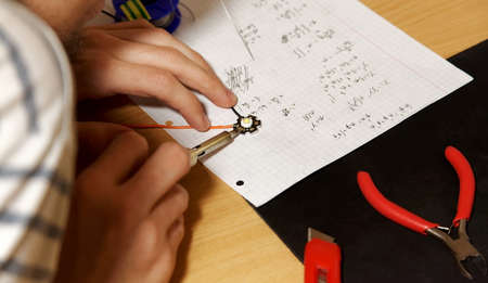 Young engineering college student soldering simple wired lambertian led diode on his desk, hands...