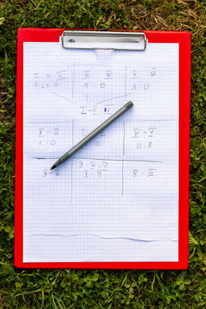 Team game paper scoreboard a pen and a holder laying on the grass outside. Numbered team results,...